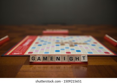 Letter tiles spelling out the words game night on stand in the foreground with out of focus game board in the background. - Shutterstock ID 1509215651
