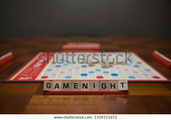 Letter\
tiles spelling out the words game night on stand in the foreground\
with out of focus game board in the\
background.