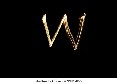 Letter W. Light painting alphabet. Long exposure photography. Drawn letter W with gold lights against black background.