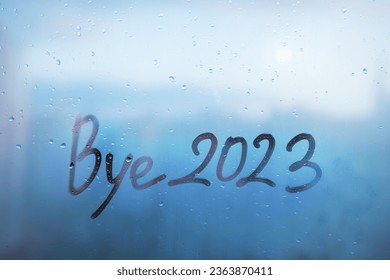 lettering bye and numbers 2023 paint with finger with streaks of water on splashed by rain foggy glass on blue window