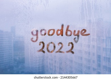 lettering goodbye and numbers 2022 paint with finger with streaks of water on splashed by rain foggy glass on blue window