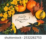 Lettering hello november on kraft paper, pen, pumpkins, autumn leaves, bouquet of yellow chrysanthemum flowers on wooden background