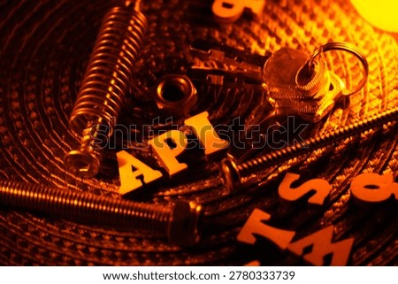 The letters API are arranged with various hardware components including screws, nuts, and a spring. A set of keys on a keyring is also visible.