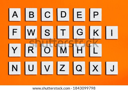 Letters of the english alphabet, a homemade wooden tile with letters on a orange background.