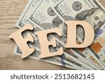 Letters Fed (Federal Reserve System) and dollar banknotes on wooden table, flat lay