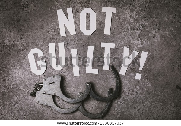 Letters with the inscription - Not guilty.\
Top view on social concept with open\
handcuffs