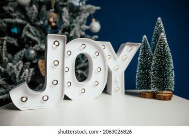 The Letters JOY Against Blue Background And Christmas Tree. Holiday Background. 