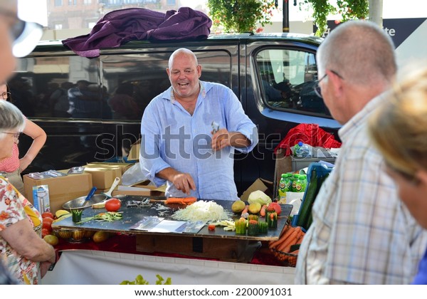 Leuven, Flemish-Brabant,\
Belgium - September 05, 2022: market vendor explains to customers\
around his stall how better the new type of knife-potato-vegetable\
peeler is