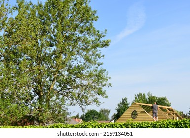 Leuven, Vlaams-Brabant, Belgium- May 22 2022: Neighbor Standing On A Ladder On A Bright Sunny Sunday Morning Building The Roof Of His Temporary Mobile Tiny House Construction Without Foundations