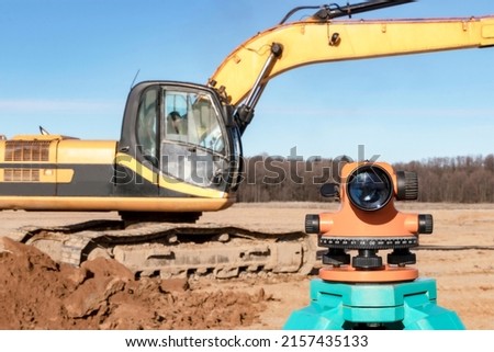 Level with an excavator in the background. Construction level or theodolite. Geodetic instruments and equipment for the construction and earthworks