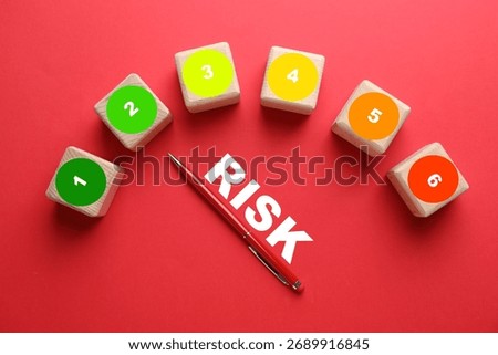 Level of risk. Pen pointing at cube with 2 on red background, top view