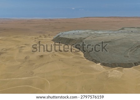 Leveled mine waste dump platform over desert dunes, panoramic aerial view