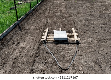Leveling the chernozem in the yard with a pallet weighted with a concrete cube, preparing for sowing the lawn. - Shutterstock ID 2311267167