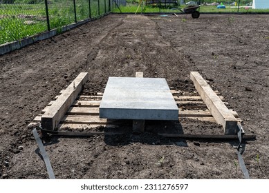 Leveling the chernozem in the yard with a pallet weighted with a concrete cube, preparing for sowing the lawn. - Shutterstock ID 2311276597