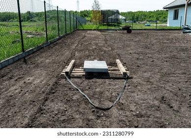 Leveling the chernozem in the yard with a pallet weighted with a concrete cube, preparing for sowing the lawn. - Shutterstock ID 2311280799