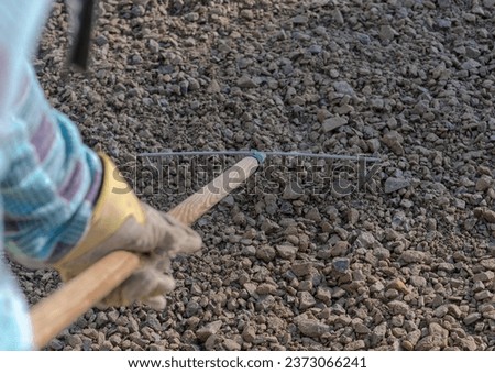 Leveling gravel (as a base for the driveway) using a rake on a wooden style (handle).A worker in a plaid work shirt and leather work gloves smooths out spilled gravel with a rake.