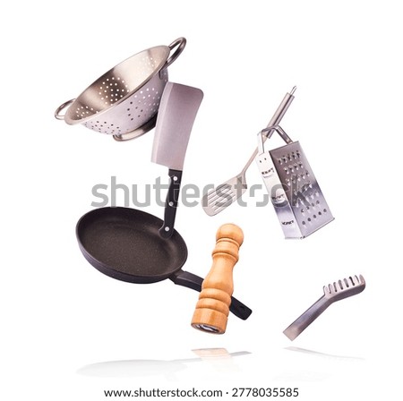 Levitating composition of flying kitchen tools including pan, colander, cleaver, and grater on a white background. Zero gravity cooking concept.