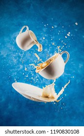 Levitating Cup, Saucer And Creamer With Splashing Plant-based Milk And Coffee On Blue Background, Selective Focus