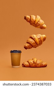 Levitating food. Crispy fresh croissants flying over coffee cup to go on brown background. Concept of food, bakery, breakfast ideas, taste, freshness. Poser. Copy space for ad
