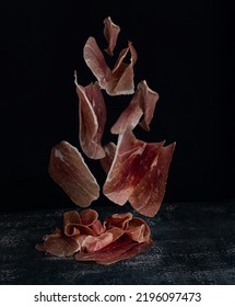 Levitating pieces of pork meat on a black background. Italian prosciutto on a dark background. Selective focus. Spanish jamon