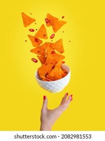 Levitation or flying of spicy hot Nachos mexican crispy crunchy tortilla chips with slices of chili pepper served as appetizer in white bowl with woman hand or palm isolated against yellow background - Shutterstock ID 2082981553