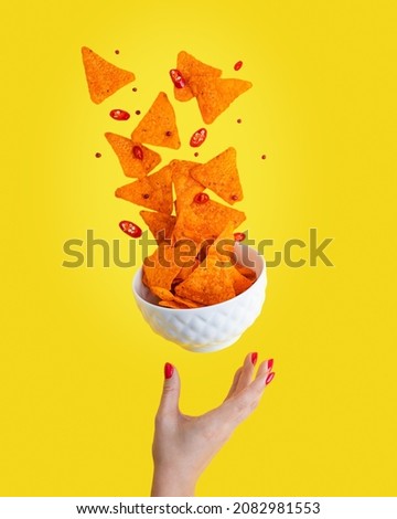 Levitation or flying of spicy hot Nachos mexican crispy crunchy tortilla chips with slices of chili pepper served as appetizer in white bowl with woman hand or palm isolated against yellow background