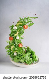Levitation or flying of vegetarian green salad made of rocket leaf or arugula, sliced cherry tomatoes, avocado slices, Mozzarella italian cheese with drops of balsamic vinegar and olive oil on plate