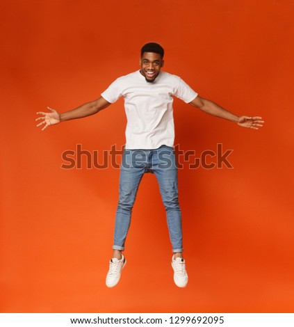 Levitation. Funny young african-american man jumping on the air, orange studio background