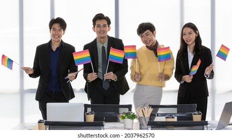 LGBT Asian executive business group smile, happy, and enjoy working together by raising symbolic rainbow flag as ally team to support transgender rights movement and community at meeting in office - Shutterstock ID 2037962570