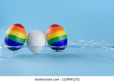 Lgbt Family. Eggs With Lgbt Flag Color And White Baby Egg On Blue Background. Creative Idea For Illustration Surrogacy Law, Right Homosexual Couple Adoption And Raising A Child.
