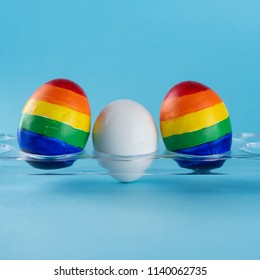 Lgbt Family. Eggs With Lgbt Flag Color And White Baby Egg On Blue Background. Creative Idea For Illustration Surrogacy Law, Right Homosexual Couple Adoption And Raising A Child.
