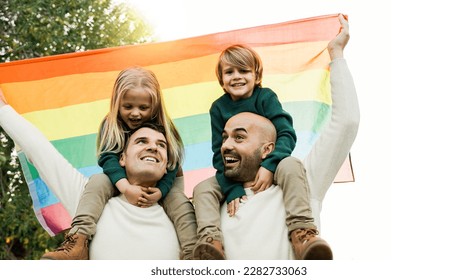 Lgbt family: Gay fathers and children celebrating with rainbow flag outdoors at park city - Diversity parents concept - Focus on dad - Powered by Shutterstock