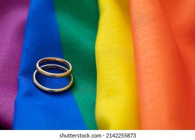 LGBT Gay Marriage. Pair Of Golden Rings On Rainbow Color Textile With Creases, Close Up View. Copy Space.