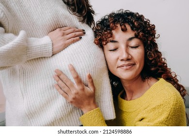 LGBT lesbian pregnant woman having tender moment listening her wife baby belly - Focus on right female