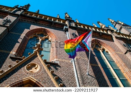 LGBT LGBTIQ+ Flag mounted on a church building waving in the wind with a clear blue sky in the background