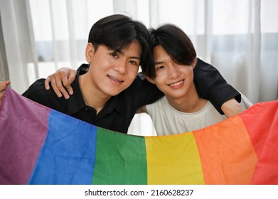 LGBT Love Couple Concept, Handsome Asian Teenage Gay Men Couple Arms Around Each Other And Holding A LGBT Rainbow Flag.