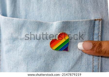 LGBT Pin in the shape of a heart on a denim jacket and a female index finger. Concept of the celebration of the LGBTQ pride flag day and people's rights.