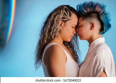 Lgbt pride concept. Gay lifestyle. Real lesbian couple hugging and kissing with iconic rainbow lgbt symbol. Prism colors of gay pride flag. Sexual orientation in young people. Transgender community.