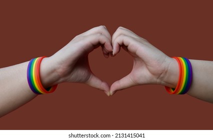 lgbt, same-sex love and homosexual relationships concept - close up of male hands with gay pride rainbow awareness wristbands showing heart gesture with clipping paths