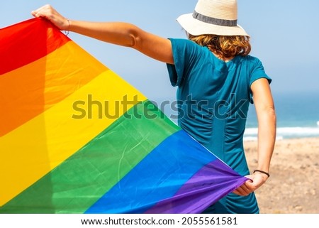 Lgbt symbol, an unrecognizable lesbian from the back in a green dress waving the flag by the sea