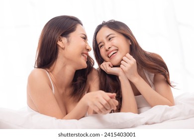 LGBTQ+ Asian couple laughing together at home. Affectionate young lesbian couple sharing a laugh while sitting on their bed at home. LGBTQ+ concept. - Powered by Shutterstock