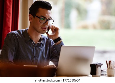 LGBTQ Community Lifestyle Concept. Young Homosexual Man Sits At The Table In Old-fashioned City Cafe. Handsome Gay Male Businessman Talks On A Phone While Having A Break At Lunch.