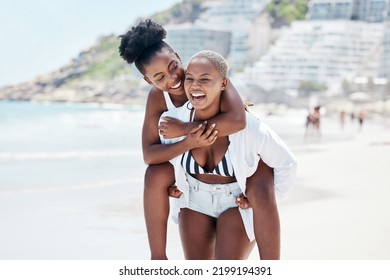 LGBTQ, gay and lesbian black women enjoying a piggyback ride and fun at beach in summer. Friends, dating and trust with female and her girlfriend on holiday, vacation or travel by the coast - Powered by Shutterstock