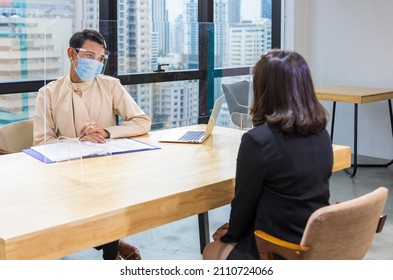 LGBTQ Manager From HR Department Wearing Facial Mask Is Interviewing New Applicant And Looking At Her Resume And Profile Through The Partition For Social Distancing And New Normal Policy