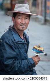 LHASA, TIBET, CHINA - AUGUST, 17 2018: Unidentified Tibetan man in traditional clothes sit on a bench nearby Jokhang temple praying with prayer wheels 