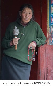 LHASA, TIBET, CHINA - AUGUST, 17 2018: Unidentified elderly Tibetan pilgrim praying with prayer wheels  in Lhasa, Tibet