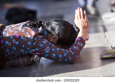 LHASA, TIBET-OCTOBER 08: A Tibetan female Buddhist pilgrim is praying in full ground prostration in front of the holy Jokhang Monastery on October 08, 2012 in Lhasa, Tibet.