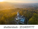 The Liberecka Vysina Lookout Tower stands majestically in Liberec, Czechia, surrounded by lush greenery as the golden sunset casts a warm glow over the landscape, inviting exploration and serenity.