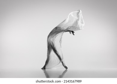 Liberty. Black and white portrait of graceful ballerina dancing with fabric, cloth isolated on grey studio background. Grace, art, beauty, contemp dance concept. Weightless, flexible actress
