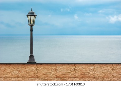 Liberty styled lamp on brick wall after raining with overcast sky and calm sea on the background